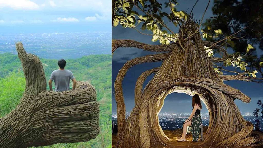 Seorang pria berdiri di atas instalasi seni berbentuk tangan raksasa dari ranting pohon di Pinus Pengger Bantul, dengan latar belakang pemandangan hijau perbukitan dan hamparan kota Yogyakarta dari ketinggian